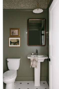 a white toilet sitting next to a sink in a bathroom under a mirror and framed pictures on the wall