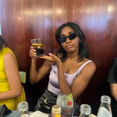 two women sitting at a table with drinks in their hands and one holding up a cell phone