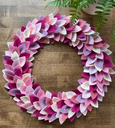 a pink and purple wreath sitting on top of a wooden table next to a plant