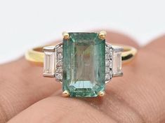 an emerald and diamond ring on someone's finger with two baguettes in the middle