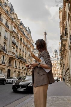 a woman is standing on the sidewalk in front of some buildings and eating bread while looking at her cell phone