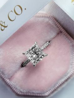 an engagement ring with a princess cut diamond on it's side in a pink velvet case