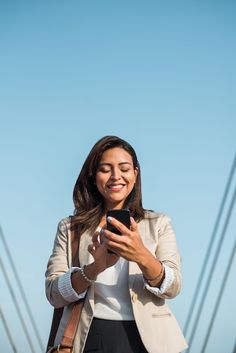 a woman is looking at her cellphone while standing in front of the golden gate bridge