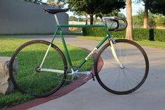 a green bike parked on the side of a sidewalk next to a stone wall and grass