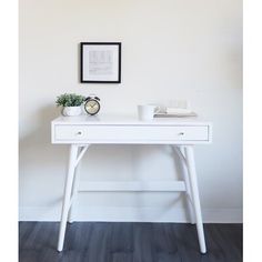 a white desk with two plants on it and a black framed picture above the table