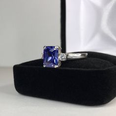 Beautiful Tanzanite* & White Sapphire Ring * 2.25ct Emerald Cut Violet Blue Tanzanite* measures 9mm x 7mm * 3.5mm Brilliant Cut White Sapphire Accents * 2.5cts Total weight * 14k White Gold * Size 9 Hallmarked & Gift Ready! Matching Earrings & Pendant Necklace is also Available! *Tanzanite is one of very few gemstones that cannot be grown in a Lab, however, these Laboratory Grown Simulate Stones are optically identical to a natural Tanzanite in color and are just as hard but, do not Blue Radiant Cut Lab-created Sapphire Jewelry, Blue Sapphire Asscher Cut Ring Gift, Asscher Cut Blue Sapphire Ring Gift, Blue Radiant Cut Cubic Zirconia Rings, Sapphire Cubic Zirconia Jewelry In Radiant Cut, Sapphire Radiant Cut Cubic Zirconia Jewelry, Sapphire Colored Cubic Zirconia Jewelry, Radiant Cut, Classic Sapphire Gemstones With Accent Stones, Blue Radiant Cut Ring With Prong Setting