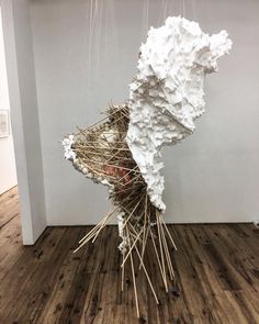 a sculpture made out of sticks and paper on top of a wooden floor next to a white wall