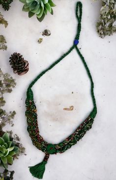 a green string necklace with beads and tassels on top of snow covered ground