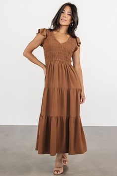 Introducing The Brandie, your new go-to choice for casual weekend brunch. With its warm medium brown hue, V-neckline, and cap-length flutter sleeves, this dress offers a relaxed yet stylish option, featuring a fully smocked bodice, natural waist, and midi-length skirt with three tiers for effortless charm. Brown V-neck Dress With Ruffle Hem, Brown Smocked Bodice Dress For Brunch, Brown Smocked Back Dress For Vacation, Flowy Tiered Brown Dress, Flowy Brown Tiered Dress, Brown Vacation Dress With Smocked Back, Flowy Brown V-neck Midi Dress, Vacation Brown Dress With Smocked Back, Brown Smocked Bodice Midi Dress For Brunch