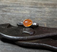 A vibrant oval Spessartite Garnet (also known as Mandarin) gemstone is set in solid 14k gold and is perched atop a sterling silver band. Perfect on its own, or a brilliant addition to your stack. Size 7.5 Garnet: 8mm x 6mm, 3.23cts Band: 2.10mm Will arrive gift-boxed. This is a natural, untreated Mandarin Garnet, not synthetic, so there will be naturally occurring inclusions. Inclusions are not considered a defect, but rather the unique personality of each stone. My jewelry is handcrafted one piece at a time by me in my home studio in Portland, Oregon. If I can help you with any questions about this piece or any of my other products, please feel free to contact me: hello @ paulla.com PIN IT on PINTEREST FOLLOW on Instagram - @paullatewksburyjewelry LIKE IT on Facebook - @paullatewksburyjew Orange Cabochon Jewelry For Anniversary, Artisan Oval Jewelry With Bezel Setting, Orange Oval Sapphire Gemstone Ring, Orange Oval Sapphire Ring, Handmade Oval Orange Jewelry, Handmade Orange Oval Jewelry, Hand Forged Oval Sapphire Ring For Anniversary, Orange Rings With Polished Finish For Anniversary, Unique Oval Orange Jewelry