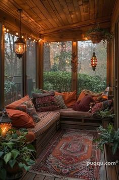 a screened porch with lots of pillows and lights on the ceiling, surrounded by potted plants