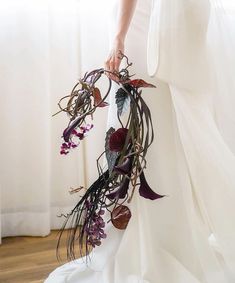 a woman in a white wedding dress holding a bouquet of dried flowers and leaves with her hands