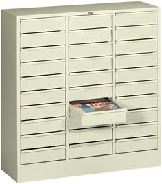 a white filing cabinet with drawers and a magazine on the bottom shelf in front of it