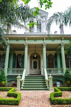 an old house with green shutters and steps leading to the front door, surrounded by greenery