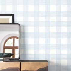 a mirror sitting on top of a wooden dresser next to a wallpapered wall