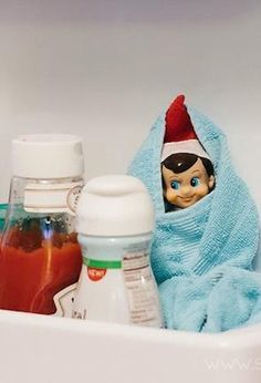 an elf doll sitting in a bathtub next to baby bottles and sauces on the sink