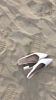 two pairs of white shoes sitting in the sand