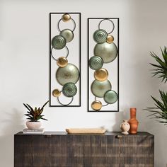 two metal art pieces hanging on the wall next to plants and potted planters