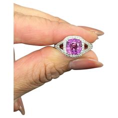 a woman's hand holding a ring with a pink stone and diamond accents on it