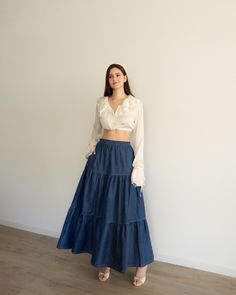 a woman standing in front of a wall wearing a white shirt and blue denim skirt