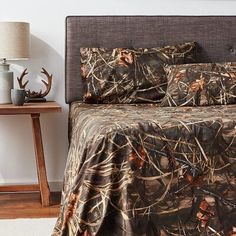 a bed covered in camo sheets and pillows with a night stand next to it