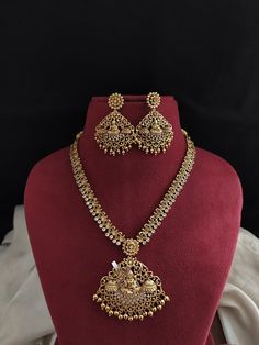 This exquisite Antique Nakshi Work Necklace Set showcases intricate craftsmanship, featuring a stunning Lord Lakshmi design. The golden drops add a touch of opulence, giving the set a real gold appearance. Paired with matching earrings, this set is perfect for traditional events, weddings, or festive occasions. Its detailed nakshi work and classic design make it a timeless addition to your jewelry collection, exuding elegance and grandeur. Temple Gold Plated Jewellery Set /South Indian Necklace / Necklace / Necklace Set/ Vintage / Bollywood Jewelry/ Indian Jewelry/Gifts. Temple Necklace set. The ruby stones are put in to enhance the beauty of the set. Comes with Golden links that will be at back to adjust the height of the necklace OR Long Haar. Perfect choice for any Indian occasion(Marri South Indian Necklace, Necklace Set With Earrings, Work Necklaces, Festival Earrings, Indian Necklace, Vintage Bollywood, Bollywood Jewelry, Festive Wear, Ruby Jewelry