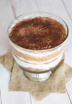 a dessert in a glass dish on top of a wooden table next to a napkin