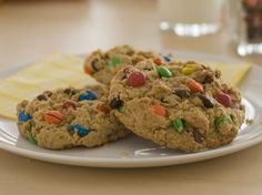 three cookies with m & m on top are sitting on a plate next to a glass of milk