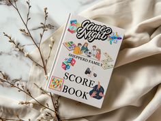 a game night book laying on top of a white sheet next to some branches and flowers