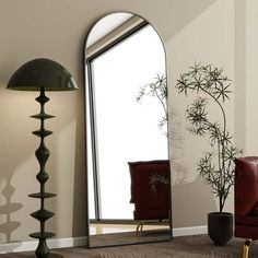 a mirror sitting on top of a wooden floor next to a red chair and lamp