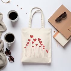 a white bag with red hearts on it next to two cups of coffee and sunglasses