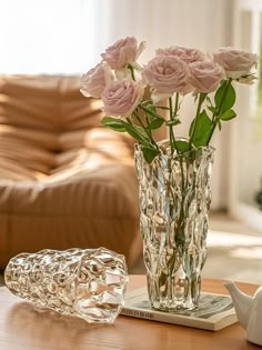 a glass vase filled with pink roses sitting on top of a table next to a teapot