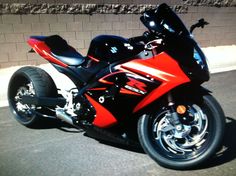 a red and black motorcycle parked on the side of the road next to a brick wall