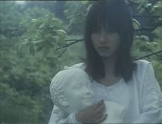 a woman holding a white statue in front of trees