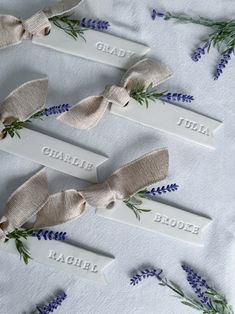 four personalized name tags with lavender flowers and ribbon tied around them on a white tablecloth