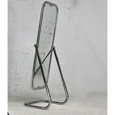 a standing mirror with a metal frame in front of a white brick wall and floor