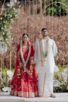 a man and woman standing next to each other in front of a gate with flowers