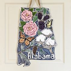 a door hanger decorated with flowers, butterflies and the state of alabama painted on it