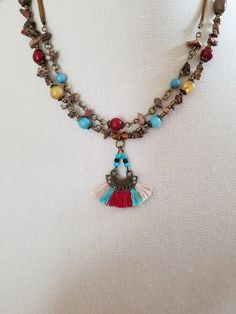 This colorful bead chip textured necklace offers small beads, imitation stone bead chips, and beautiful suede cord details. The necklace measures 17 inches and includes a 3-inch extender piece. The multi-color fan tassel pendant sports a tribal-style metal setting with triangular cutouts, seed bead details, and fabric tassels in beige, red, and turquoise. This unique southwestern tribal necklace is sure to please! Adjustable Bohemian Tassel Necklace With Colorful Beads, Southwestern Style Multicolor Necklaces With Dangling Beads, Multicolor Artisan Jewelry With Tassels, Adjustable Multicolor Beaded Tassel Necklace, Artisan Multicolor Tassel Jewelry, Bohemian Multicolor Jewelry With Lobster Clasp, Multicolor Bohemian Beaded Necklace, Adjustable Multicolor Tassel Necklace With Colorful Beads, Adjustable Beaded Tassel Dangle Necklace