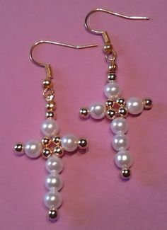 a pair of cross earrings with pearls hanging from it's earwires on a pink background