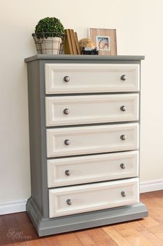 a white dresser sitting on top of a hard wood floor next to a potted plant