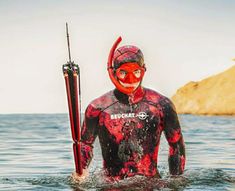 a man in a red and black wet suit holding a pole while standing in the water