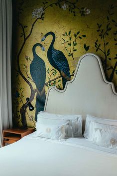 a bed with two birds painted on the wall behind it and another bird sitting on the headboard