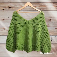 a green knitted sweater hanging on a hanger against a wooden wall with wood planks in the background