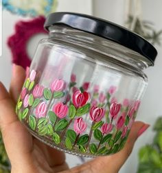 a hand holding a glass jar with flowers painted on it