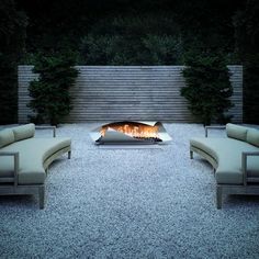 an outdoor fire pit in the middle of a gravel area with couches and chairs around it