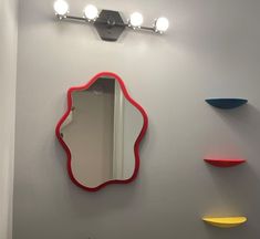 there is a mirror on the wall with lights above it and three shelves behind it