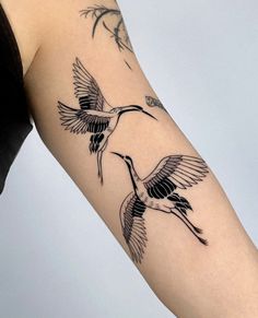 a woman's arm with two birds flying in the air and one bird on it