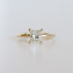 a yellow gold engagement ring with a princess cut diamond in the center, on a white surface