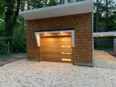 two garages with one open and the other closed in front of them on gravel area next to trees